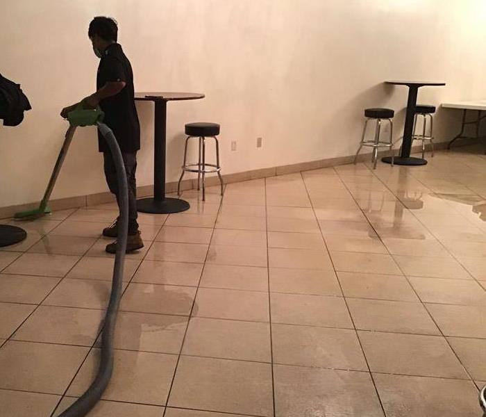 large room with standing water and man using vacuum to clean water