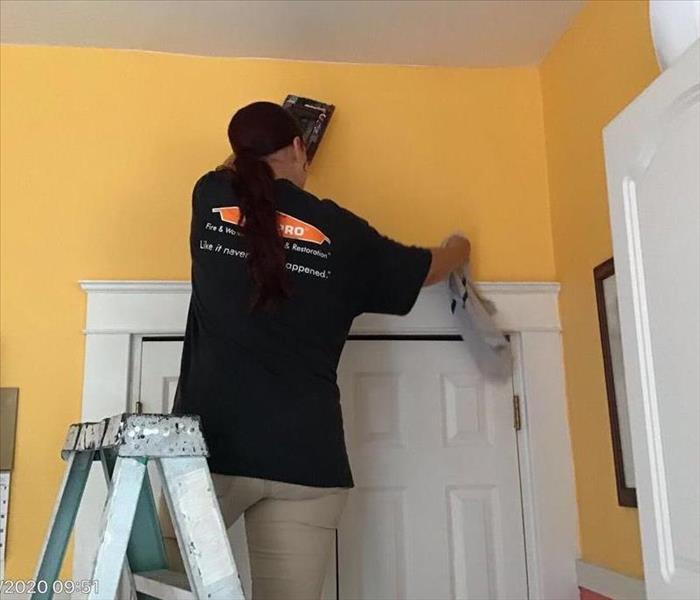 female SERVPRO employee on ladder wiping down orange wall with a rag 