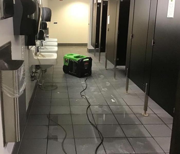 public restroom with water on floor and SERVPRO dehumidifier 