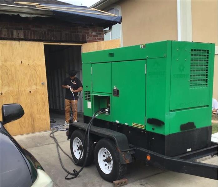 SERVPRO employee standing between garage boarded up and green generator 