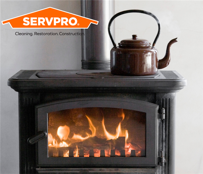wood burning stove with tea kettle on top of it. SERVPRO Logo in top left corner.