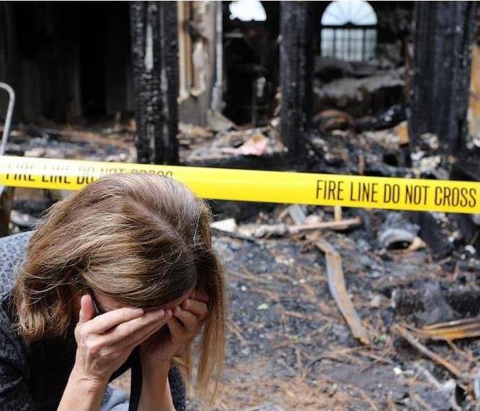 woman with her face in her hands upset in front of a house fire